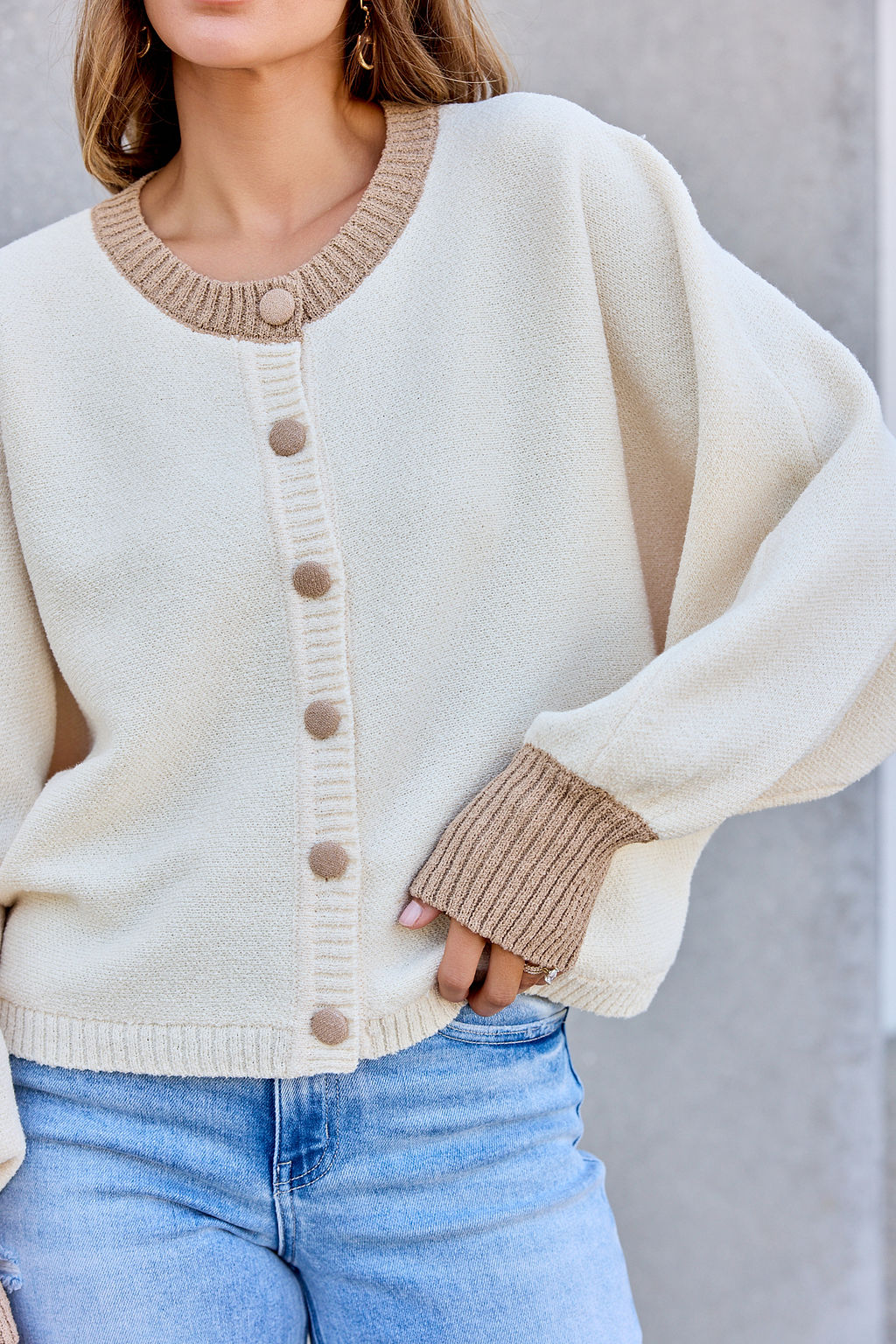 Woman in Contrast Ribbed Cardigan - Cream with tan trim and light blue jeans, standing against a gray background.