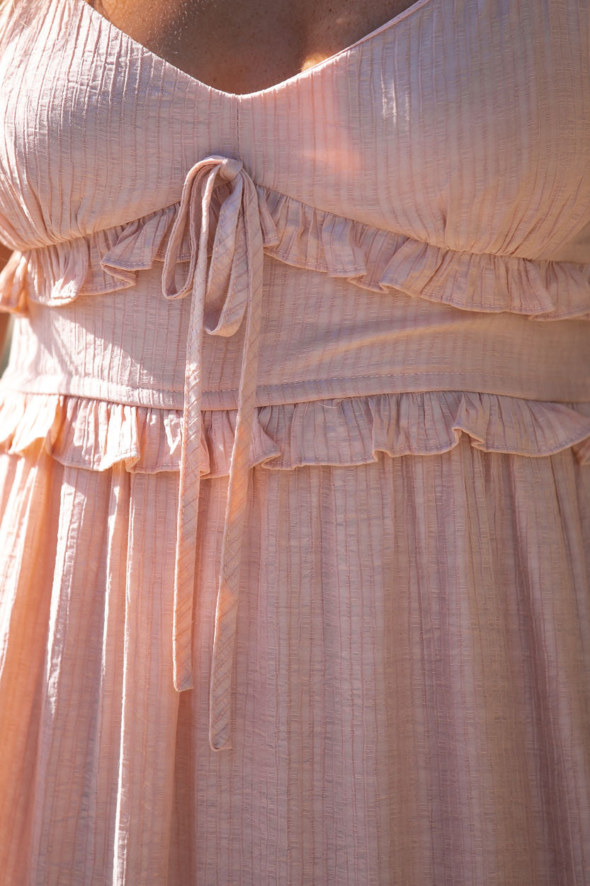 Close-up of the Dusty Pink Blossom Tiered Midi Dress with chest tie, ruffled tiers, and sunlight highlighting its delicate texture.
