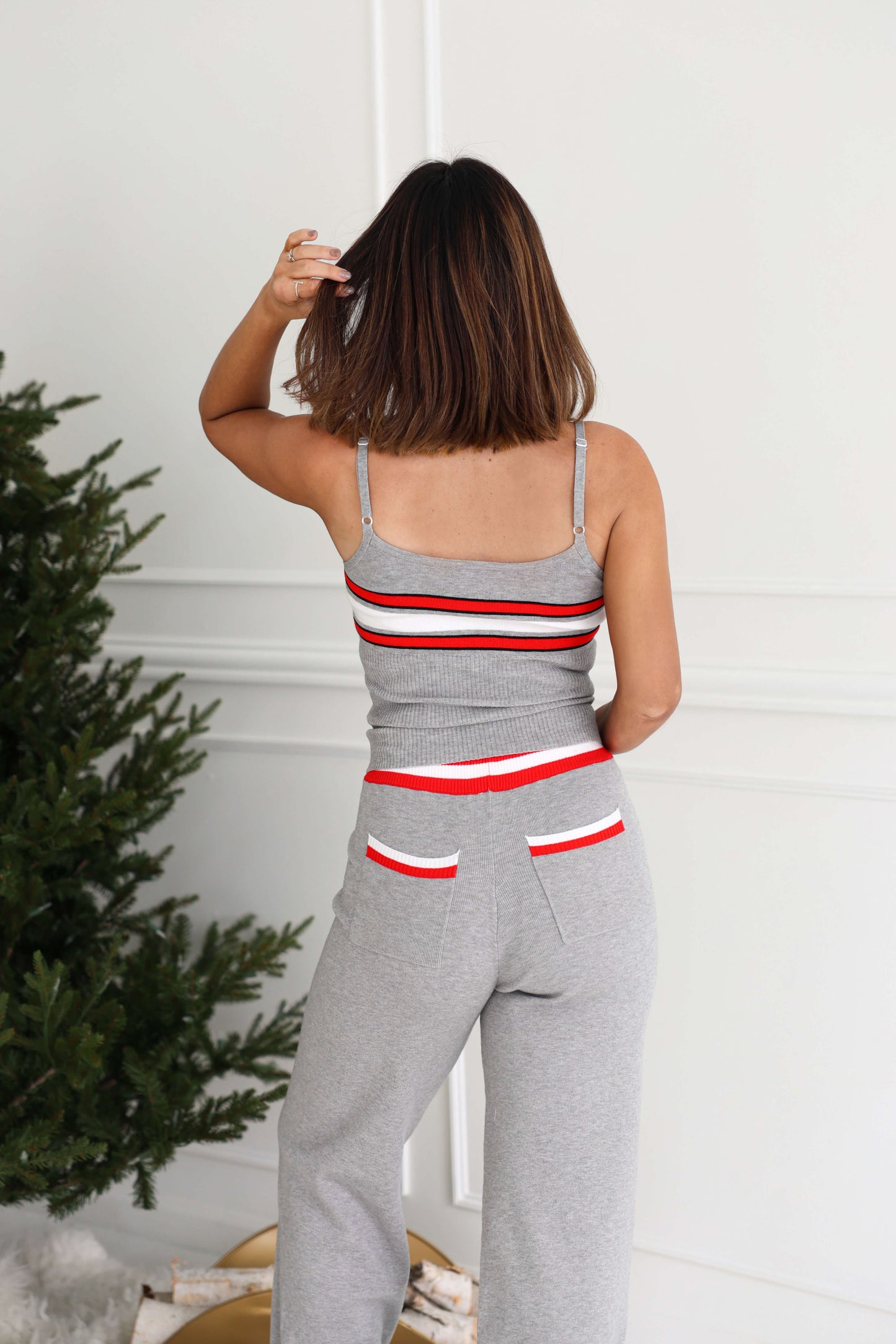 A woman wearing a Grey Striped Rib Knit Tank Top stands with her back to the camera near a decorated evergreen tree.