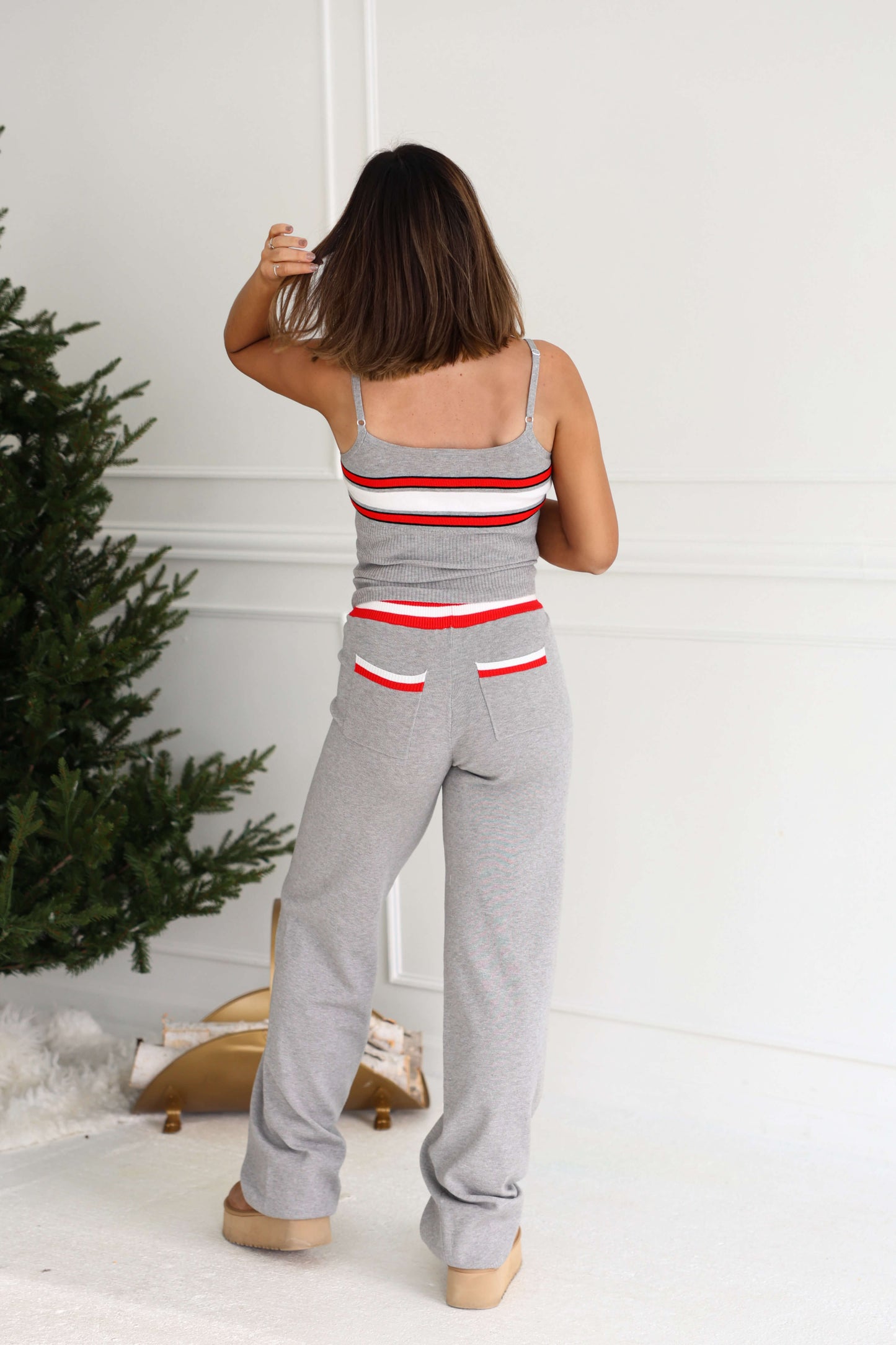 A woman in Grey Striped Drawstring Pants stands indoors by a Christmas tree, facing away and brushing her hair.