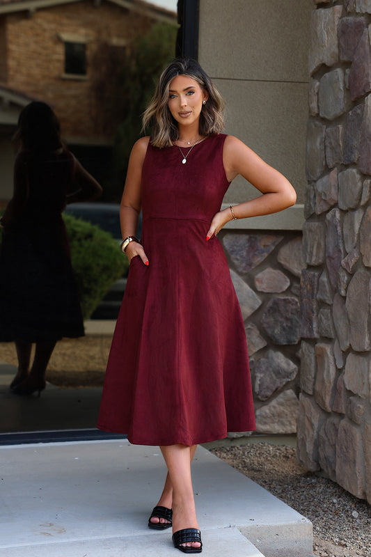 A woman stands outdoors wearing a Sleeveless Round Neck Midi Dress - Garnet, a sleeveless, garnet-colored midi dress with pockets.