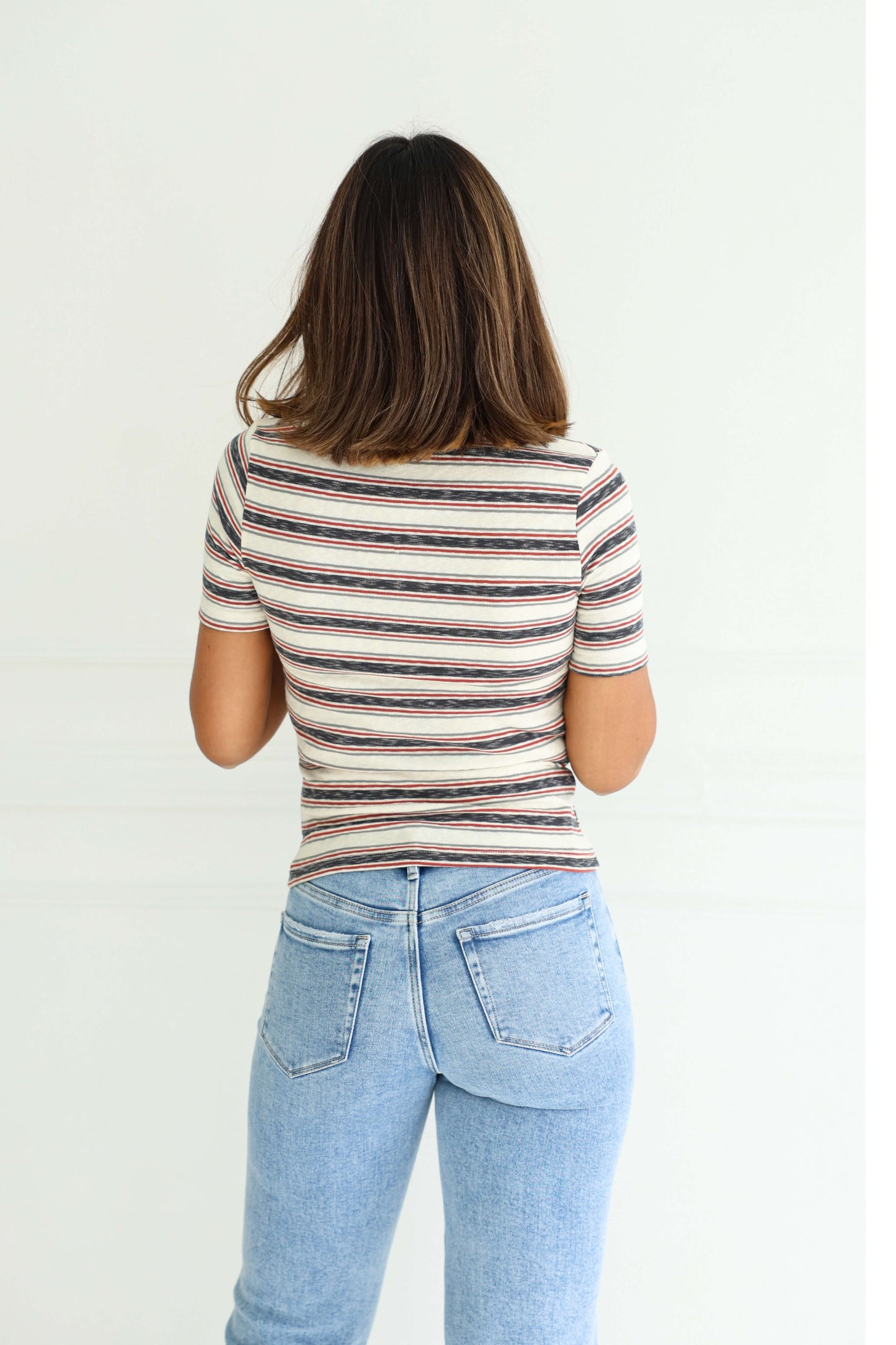 A woman with shoulder-length brown hair models the Ivory Contrast Striped Rib Polo Top, standing with her back to the camera.