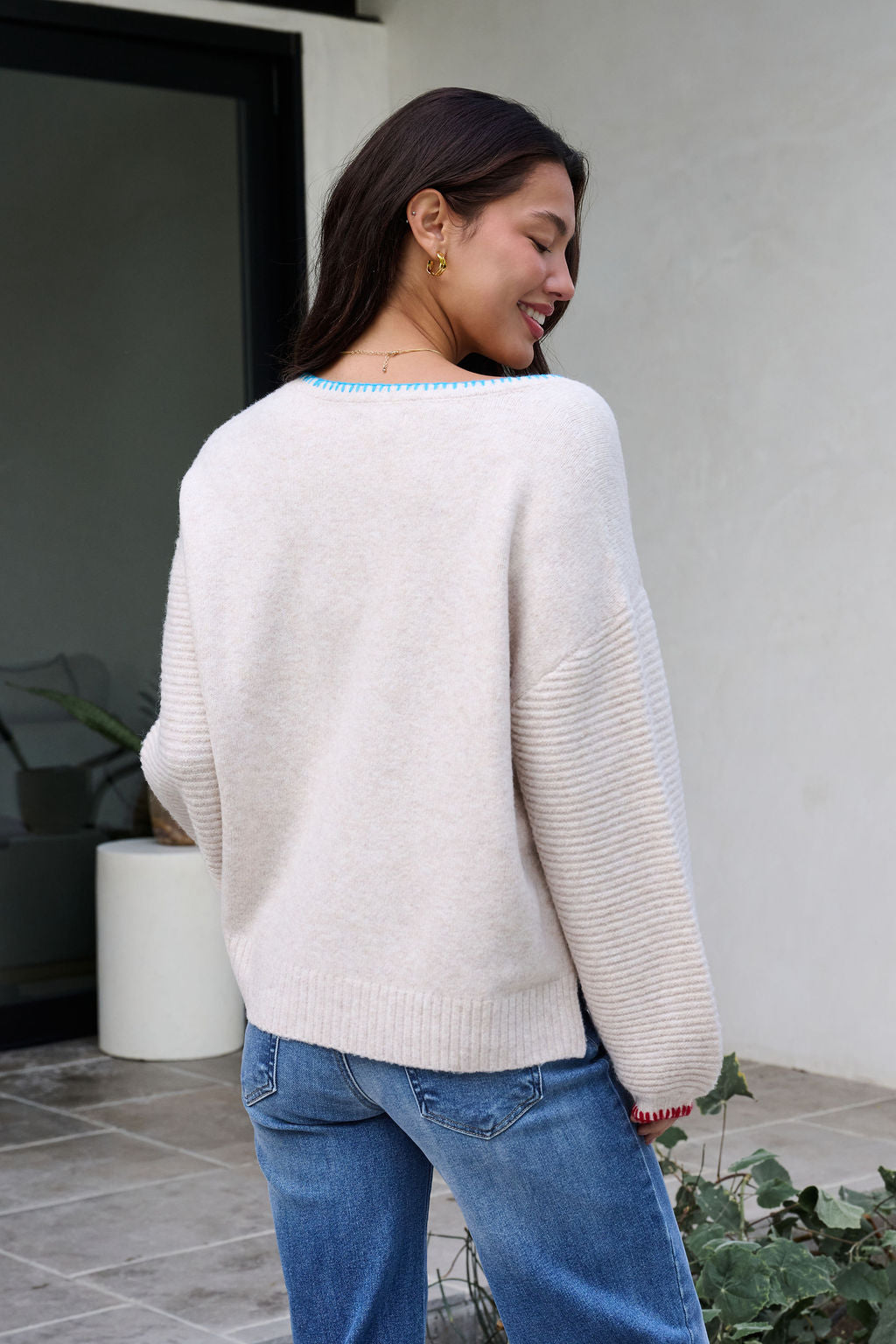 Woman outside in an Ivory Stitch Trim Button Up Sweater and blue jeans, smiling with her head turned to the side.