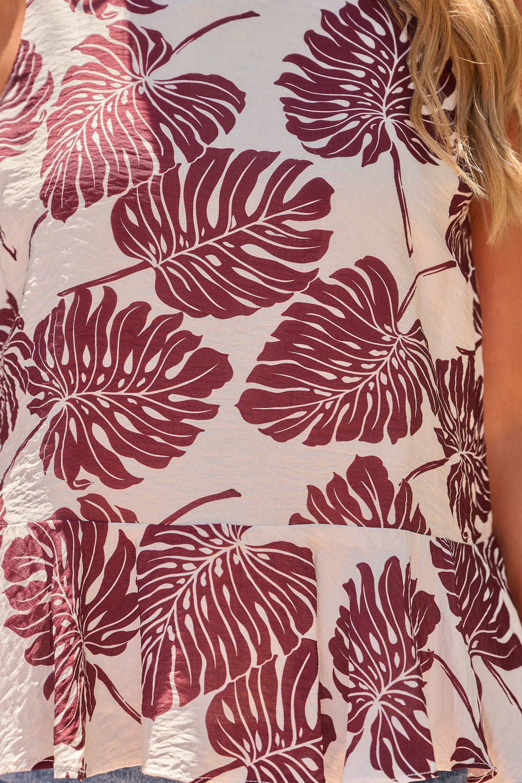Close-up of The Palm Ruffle Top - Brown with a maroon botanical print and ruffle hem, worn by a long-haired blonde model.