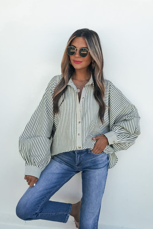Woman in sunglasses wears Loose Ends Striped Shirt - Olive, styled with blue jeans, against a white background.