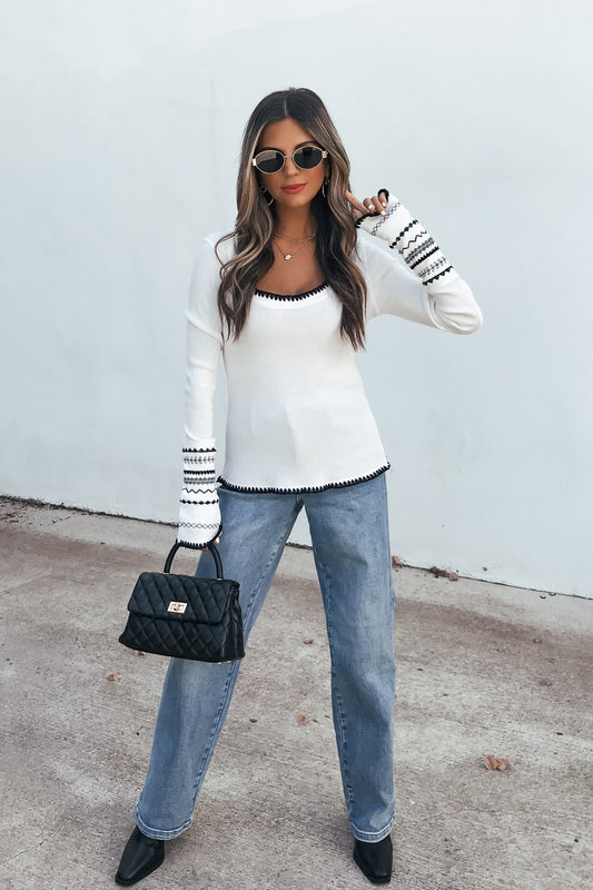 Woman in Free People Aspen Thermal Top - White, blue jeans, and black quilted bag stands by a white wall.