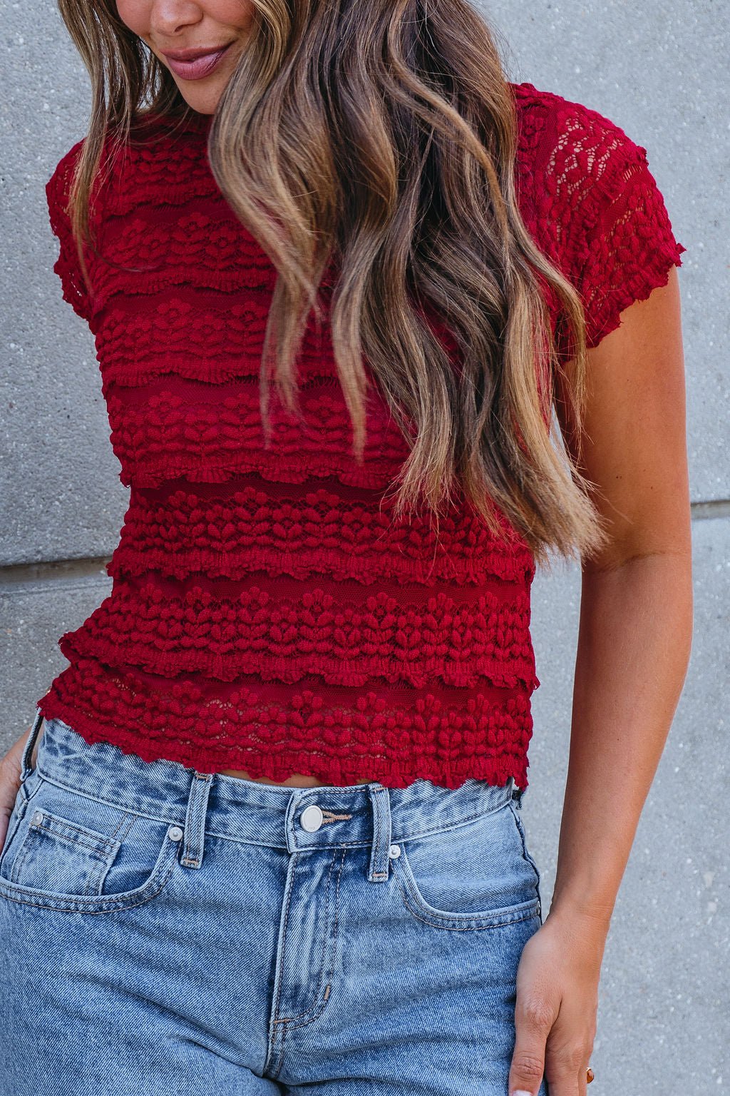 Woman wears the Amara Burgundy High Neck Lace Top with blue high-waisted jeans—perfect for your fall wardrobe.