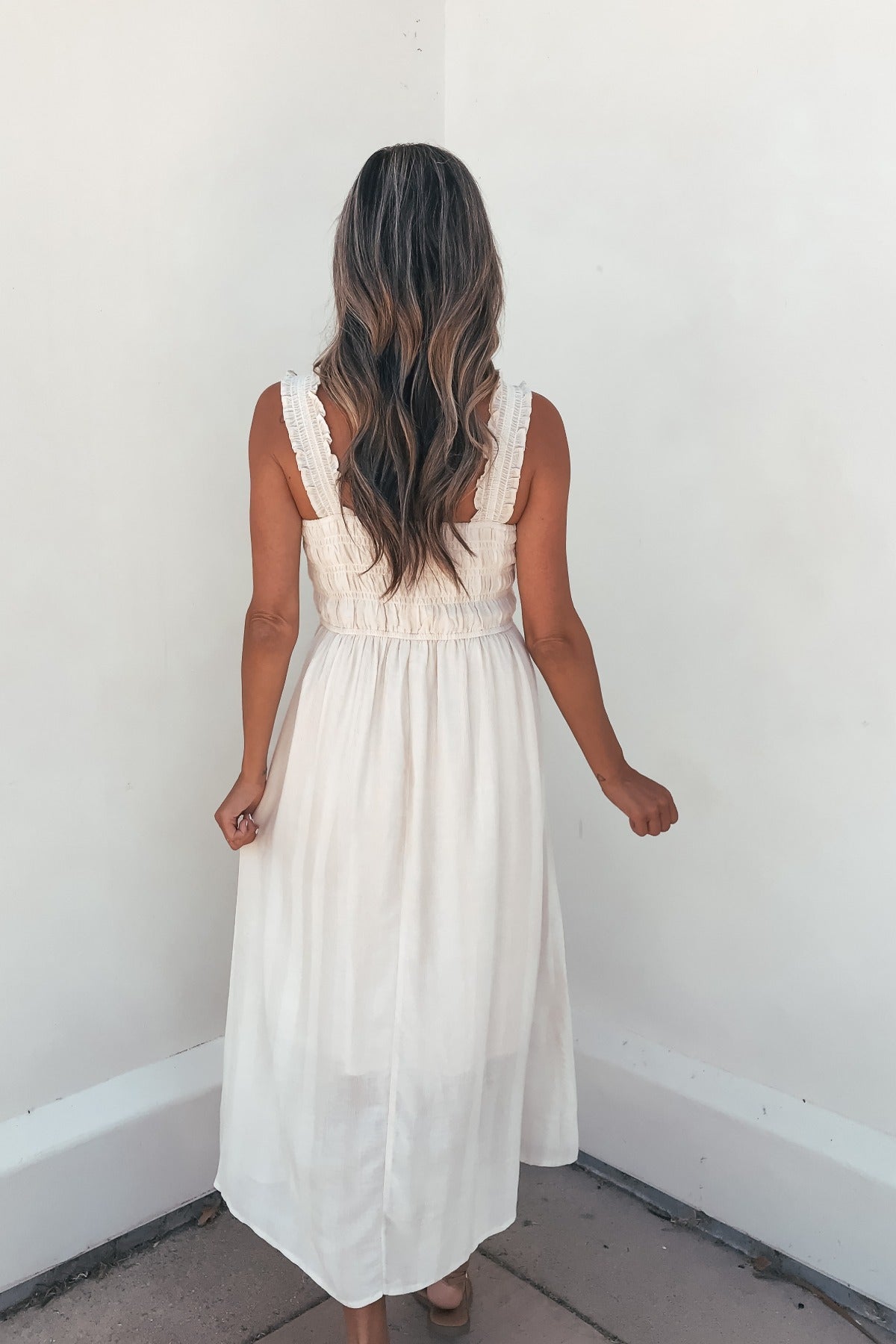 Woman with long wavy hair in the Arwen Ruffle Smocked Midi Dress - Natural, seen from behind.