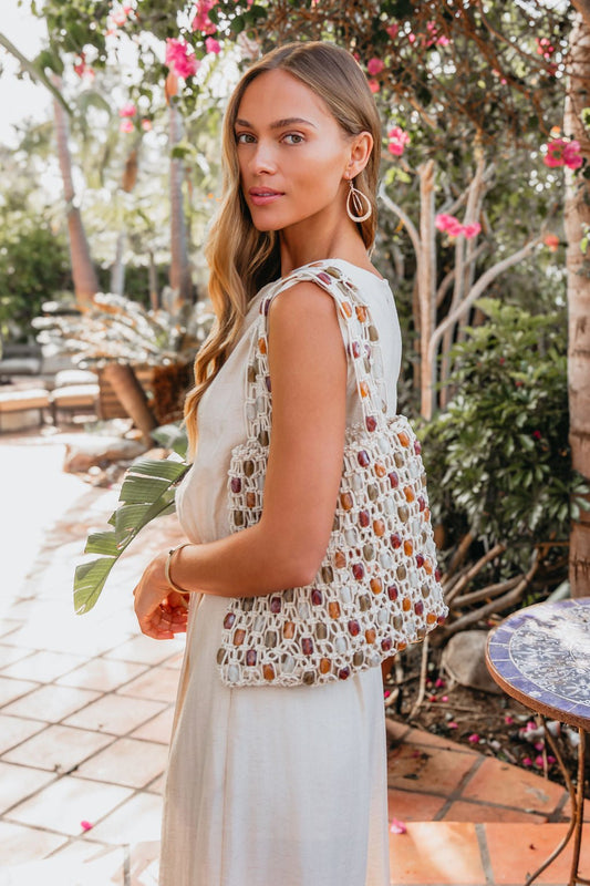 Woman in a white dress holds the Asher Multi Beaded Tote Bag outdoors, surrounded by greenery and pink flowers.