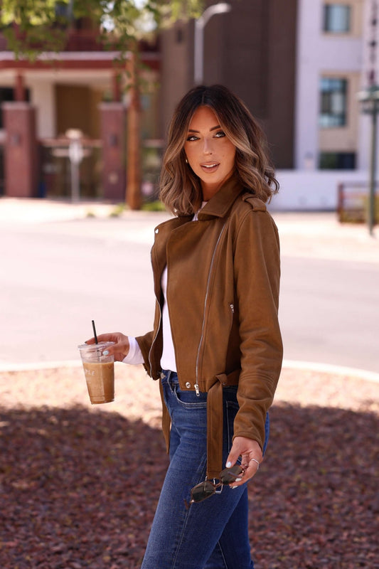 Woman in the Audrey Taupe Vegan Suede Moto Jacket holds iced coffee and sunglasses while walking outdoors on a sunny day.