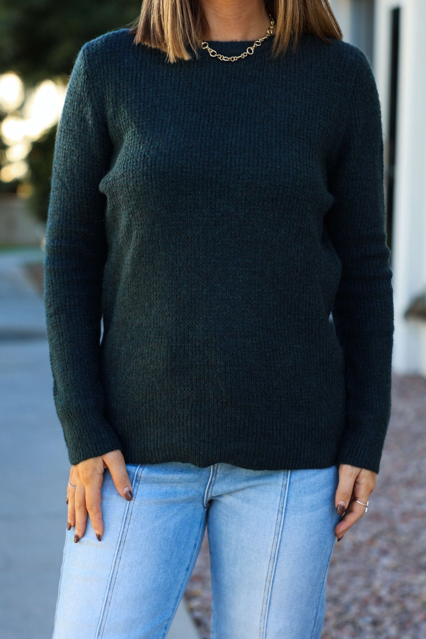 A woman stands outdoors in the Autumn Glow Brushed Teal Waffle Knit Sweater and light blue jeans, hands relaxed by her sides.