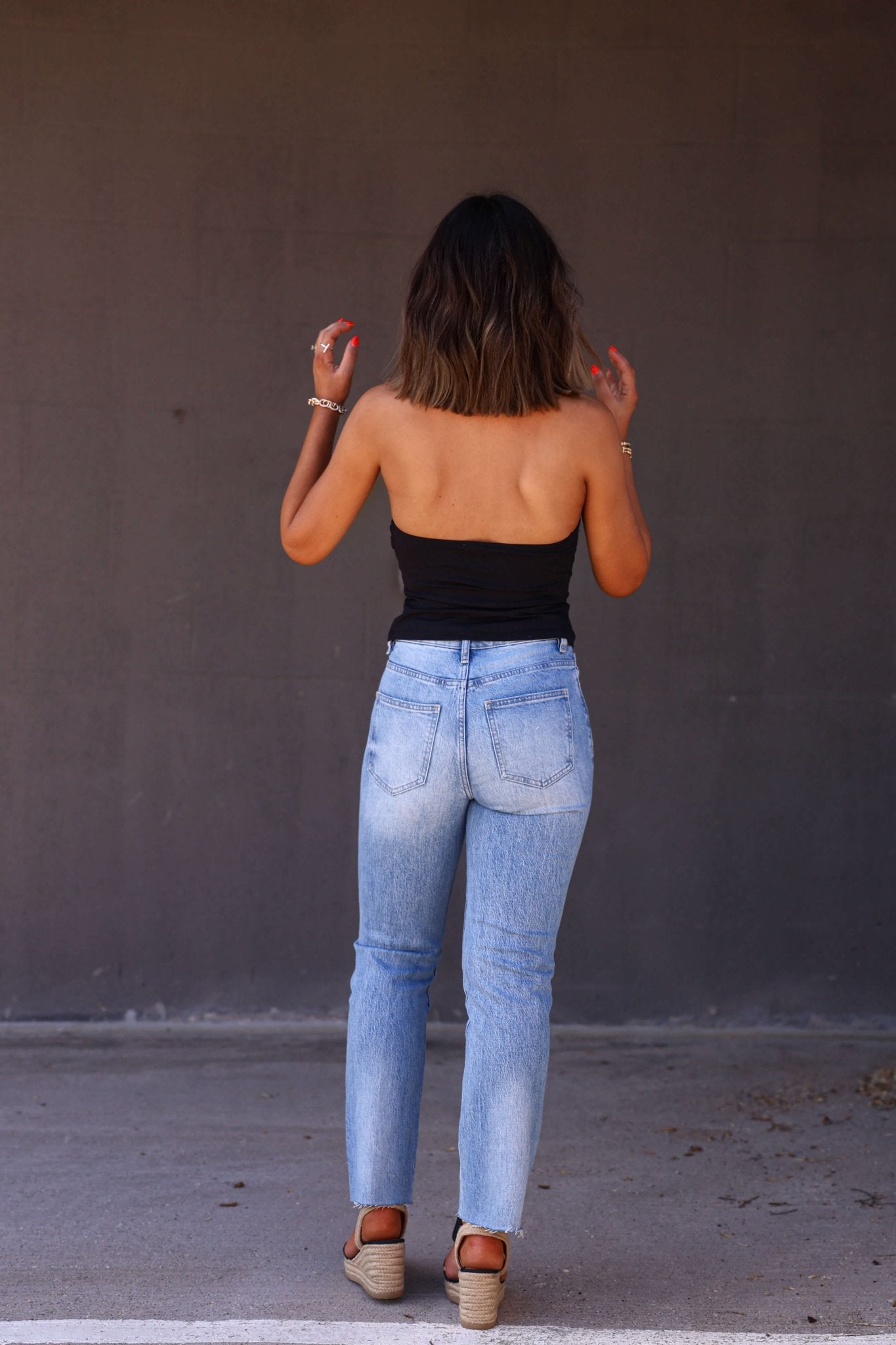A woman faces a dark wall with her back to the camera, wearing Bayeas Medium Wash High Rise Straight Jeans and a black strapless top.