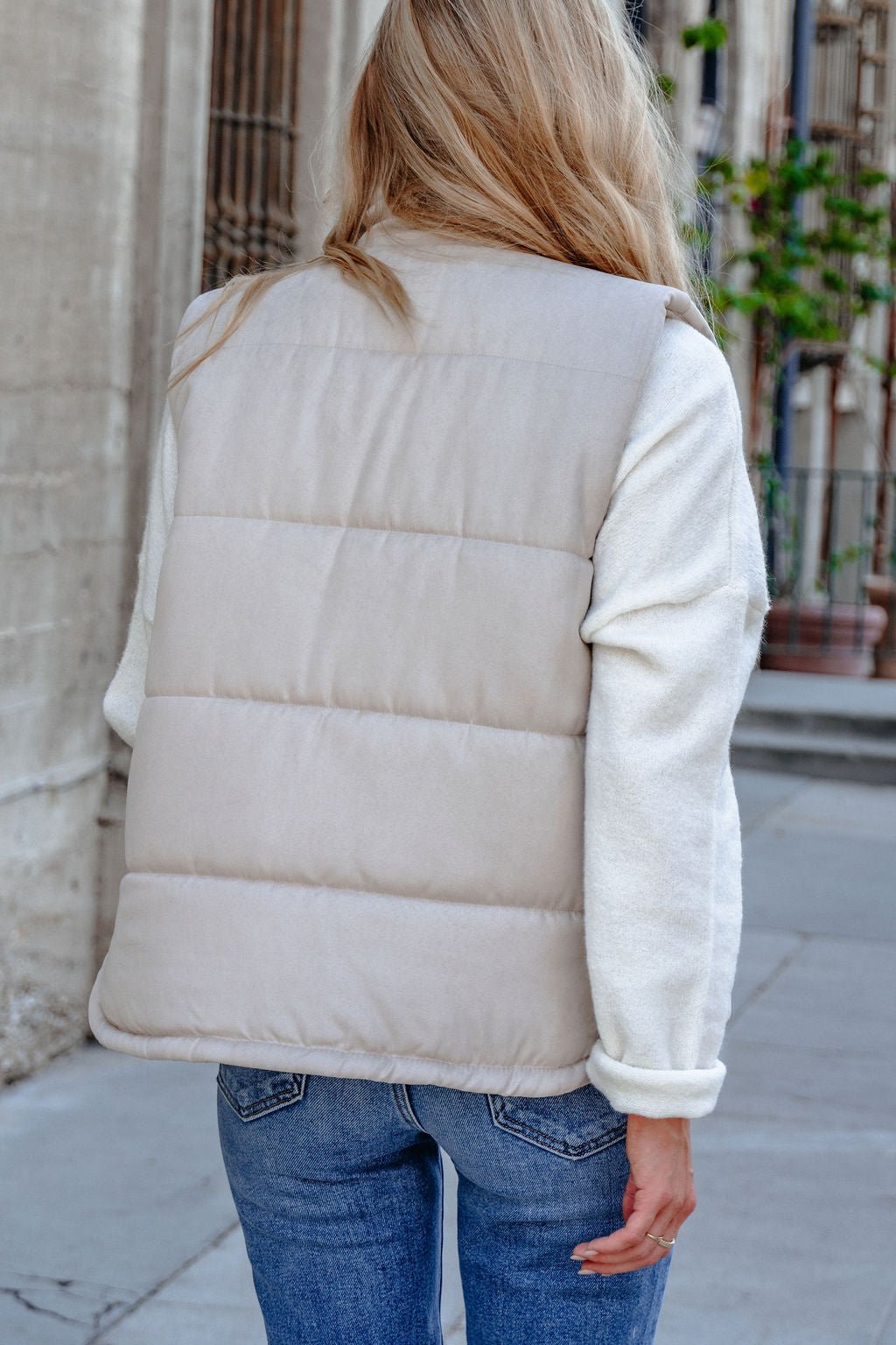 A person in a Beige Button Up Puffer Vest and jeans models fall layering while strolling down a city sidewalk.