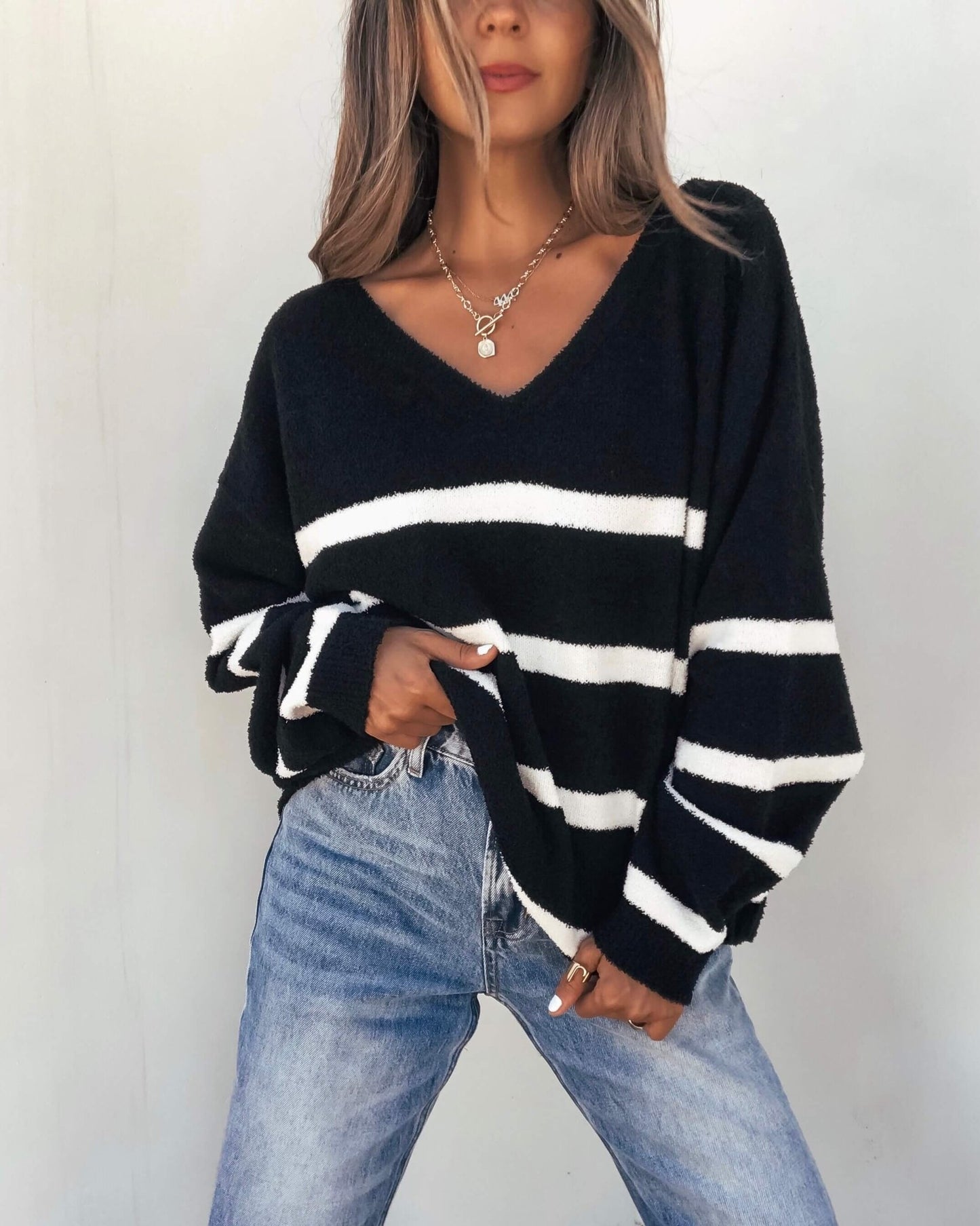 Woman models a Black and White Striped V Neck Sweater with blue jeans against a plain light background for a chic fall look.