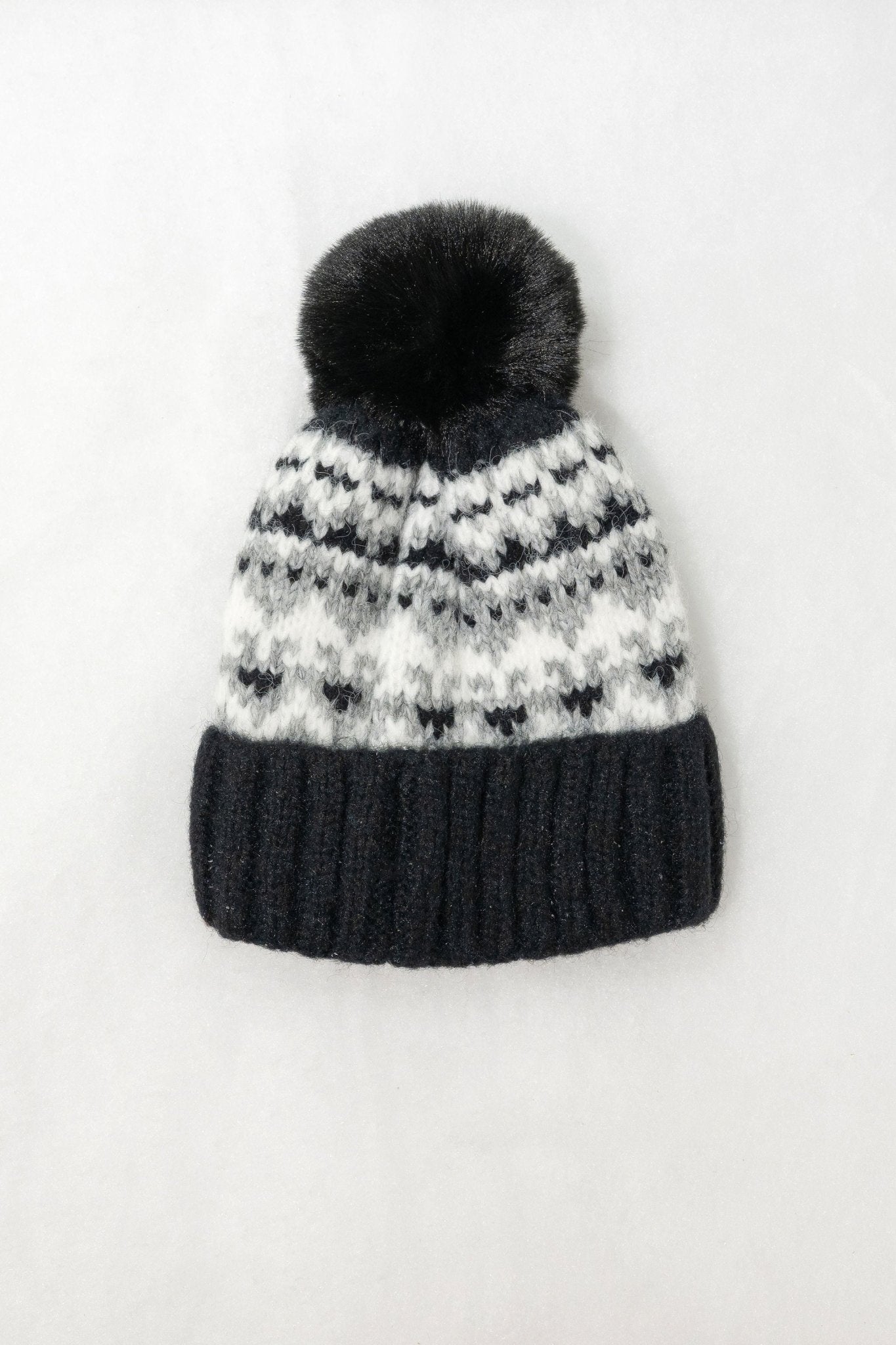The Black Aztec Pom Beanie features a dark pom-pom, black and white pattern, and thick ribbed brim on a white background.