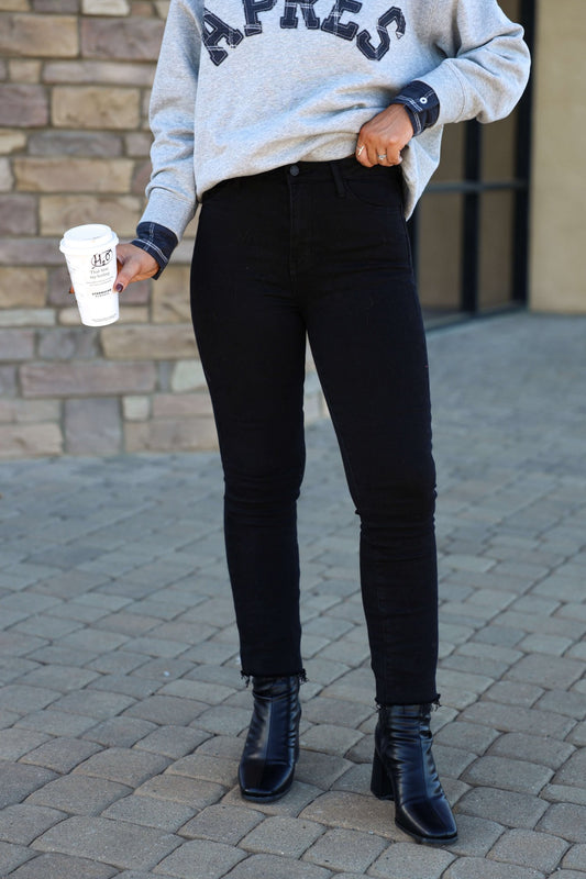 Wearing Black Frayed Hem Straight Leg Jeans - FINAL SALE, person holds a coffee cup and stands on a walkway in black heeled boots.