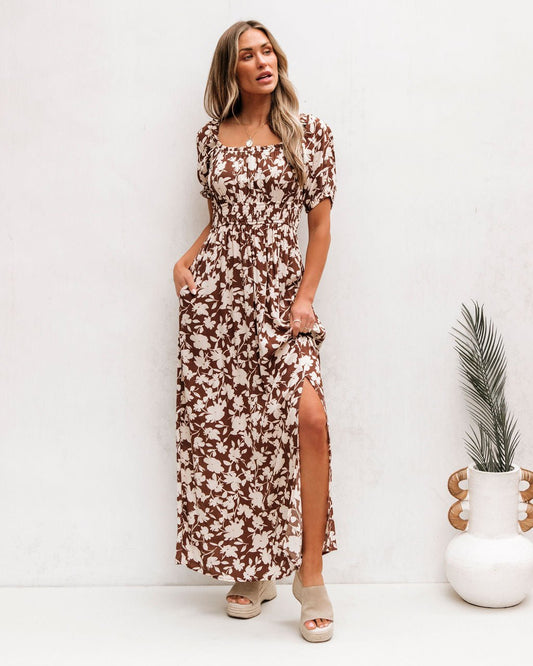 Woman wears Brown Floral Print Slit Maxi Dress with short sleeves and leg slit, paired with beige sandals against a white background.