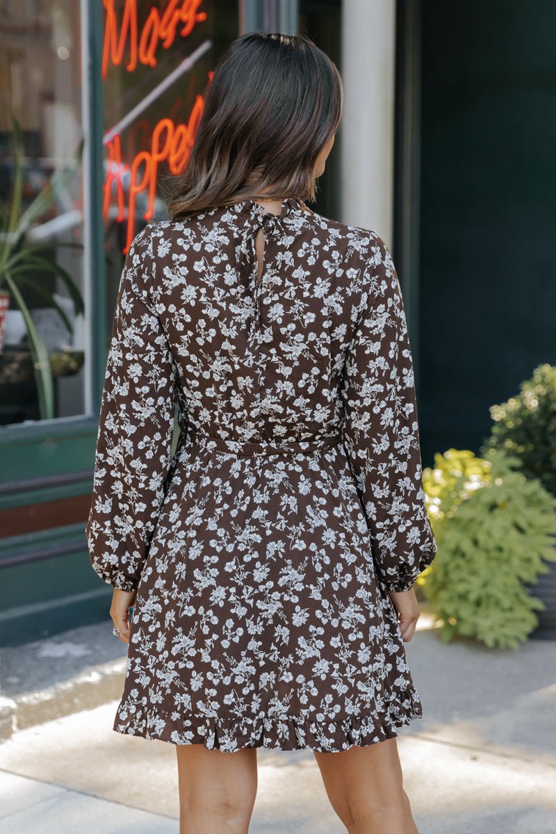 Woman stands outside in the Brown Floral Tie Waist Mini Dress - FINAL SALE, featuring a keyhole back—perfect for fall.