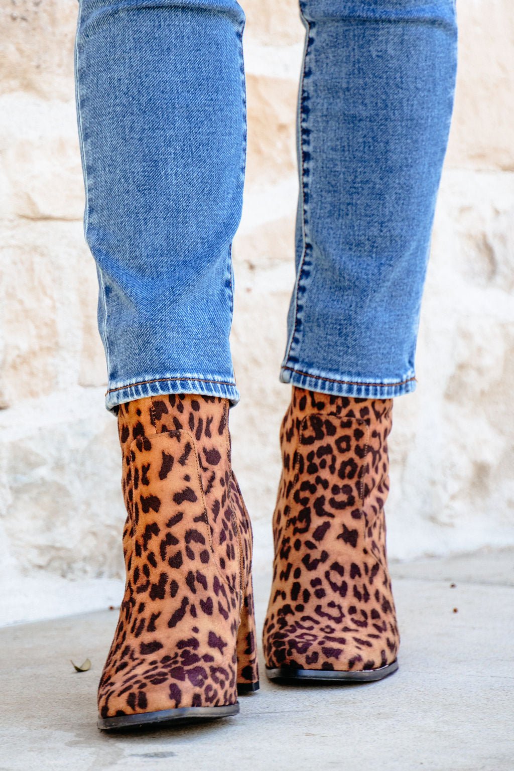 Person in blue jeans and brown leopard suede booties standing on a light-colored surface.