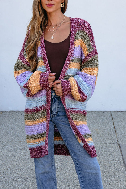 Woman in a bump-friendly Burgundy Striped Open Front Cardigan over a brown top and blue jeans, standing outdoors by a plain wall.