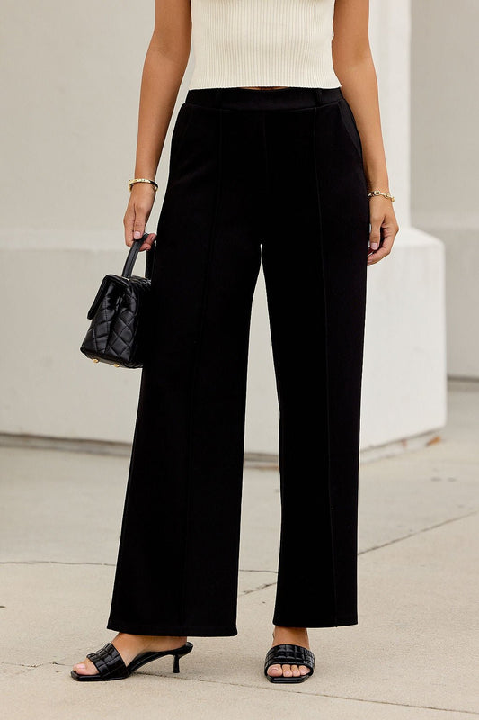 Woman wearing Buttery Soft Dress Pants - Black, cream sleeveless top, black heeled sandals, and a small quilted handbag.