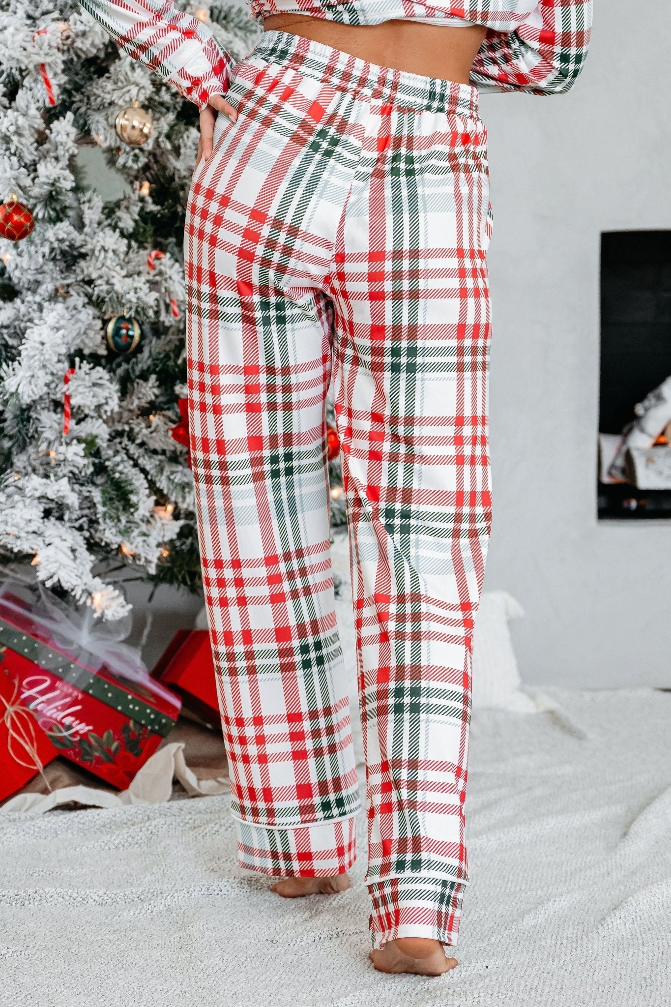 A person in the Buttery Soft Red and Green Plaid Pajama Set stands barefoot by a decorated Christmas tree and presents.