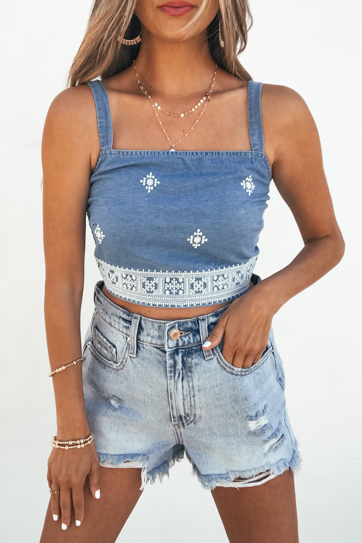 Woman in a Chambray Diamond Shape Eyelet Smocked Tank Top and distressed denim shorts, styled with layered necklaces and bracelets.