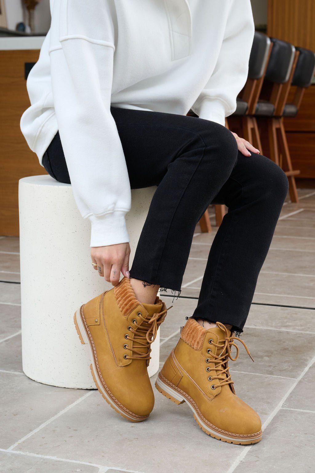 Wearing a white sweatshirt and black jeans, someone touches their Chinese Laundry Camel Alpine Faux Leather Boot.