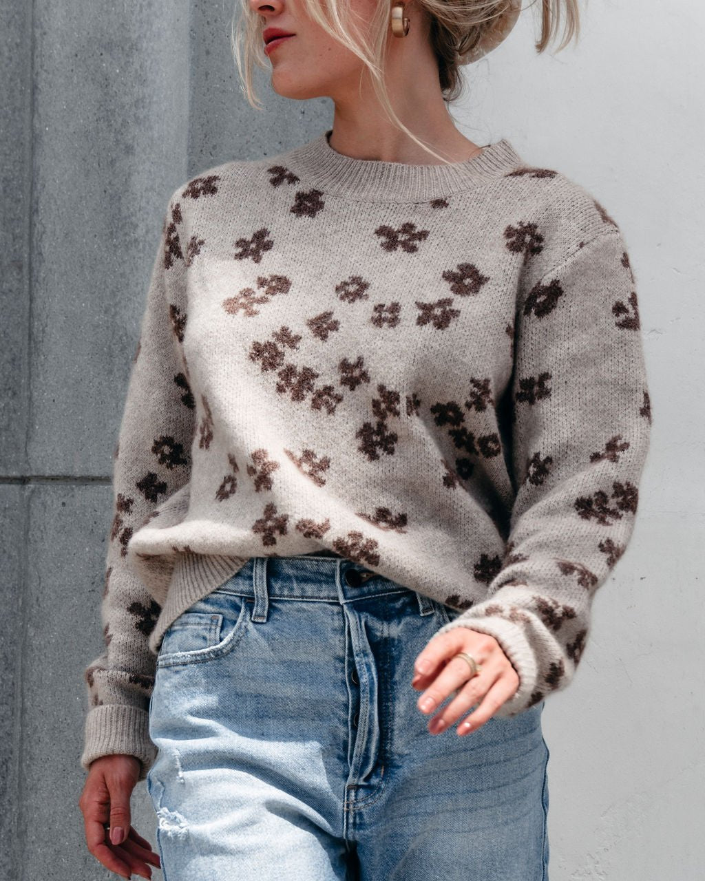 A woman in the Chunky Daisy Print Sweater - Mocha stands against a light wall—perfect for your fall wardrobe.