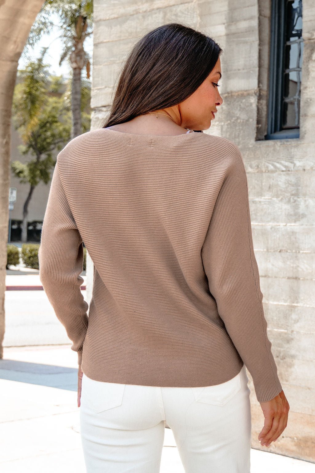 A woman in a Cozy Ribbed Boat Neck Sweater - Mocha and white pants stands outdoors, showcasing fall-ready style.
