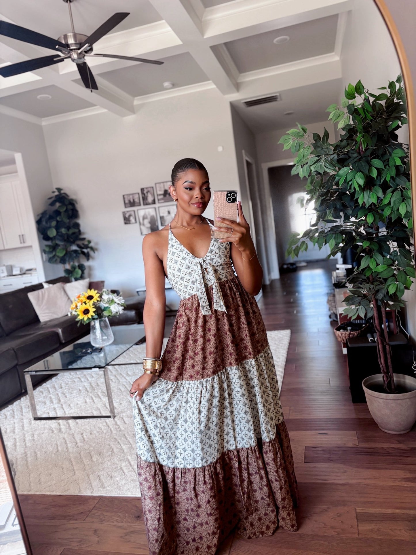 Woman wears a Cream Color Block Halter Maxi Dress and takes a mirror selfie in a stylish living room with plants and sunflowers.