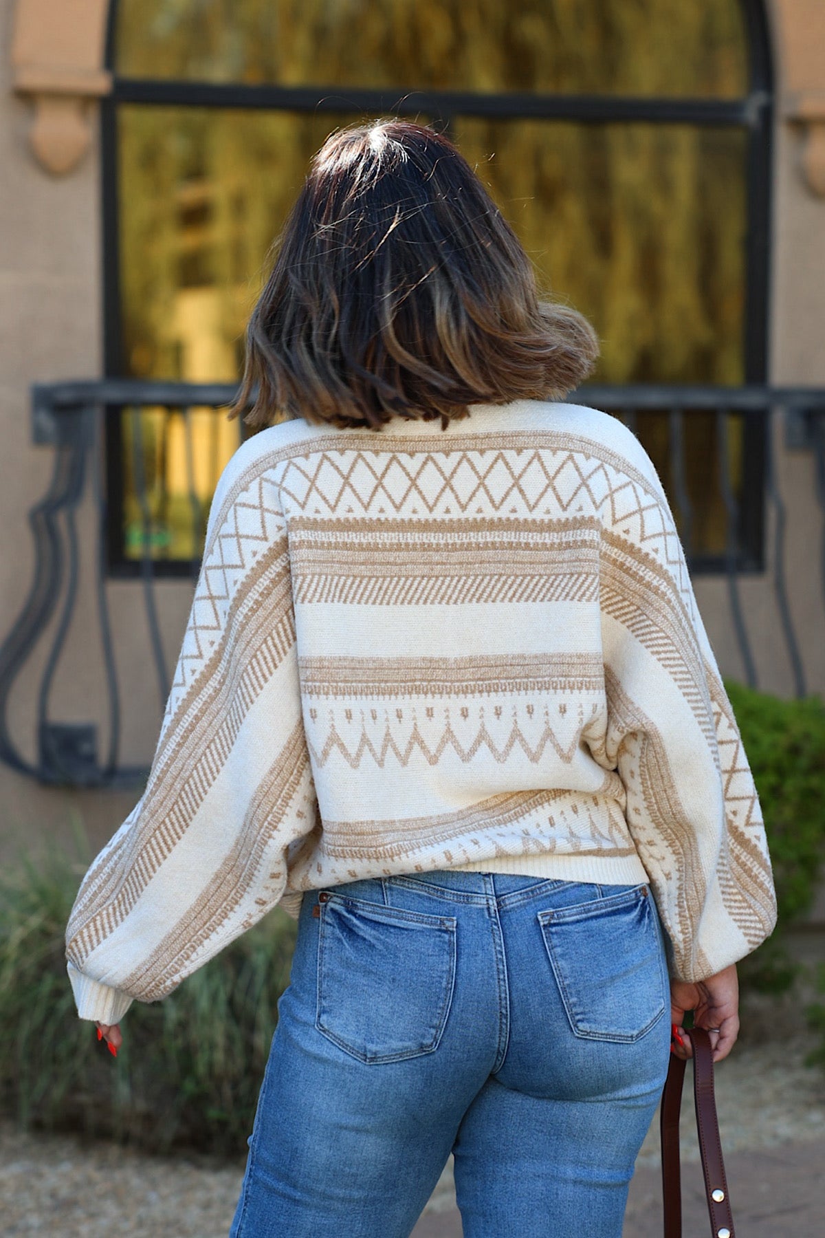 Woman with shoulder-length brown hair wears the Cream Print Long Sleeve Sweater and jeans, standing outdoors facing away.