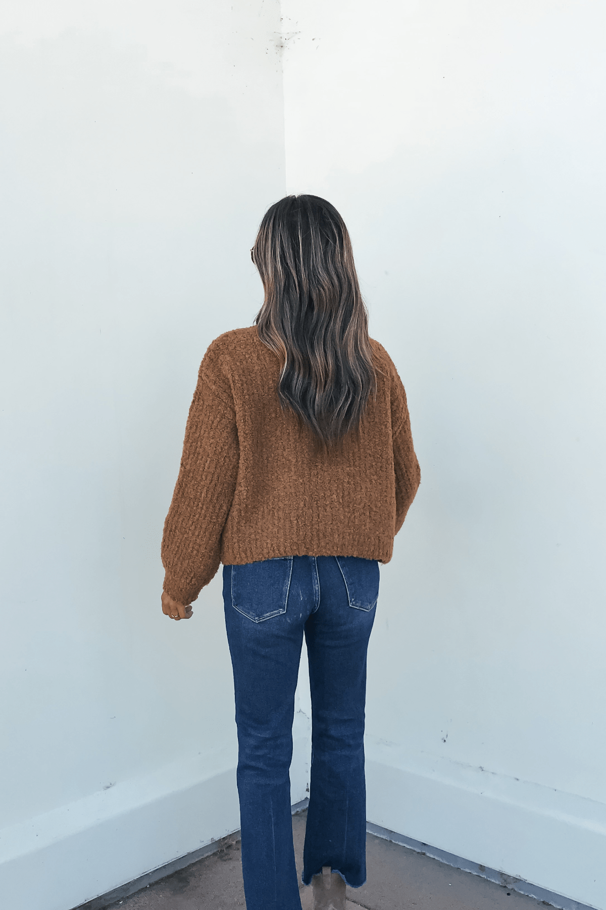 A person with wavy brown hair wears the Dark Amber Plush Button Down Cardigan, standing in front of a white wall.