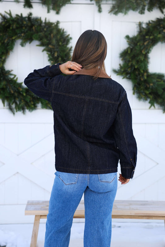 Facing away, a person with straight brown hair wears the Dark Denim Carpenter Jacket - FINAL SALE and light blue jeans by green wreaths.