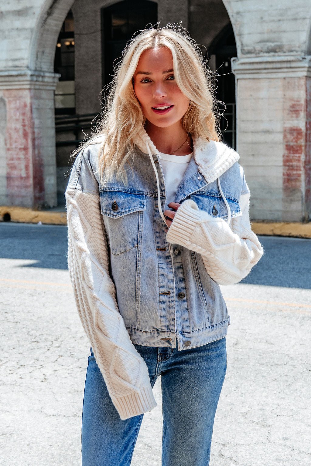 A woman wears the Elan Denim Hooded Sweater Jacket with cable knit sleeves, smiling outdoors on a city street.