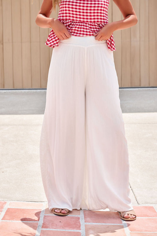 Person in a red gingham sleeveless top and Elan Flowy Wide Leg Pants - Ivory, standing outdoors on a tiled surface.