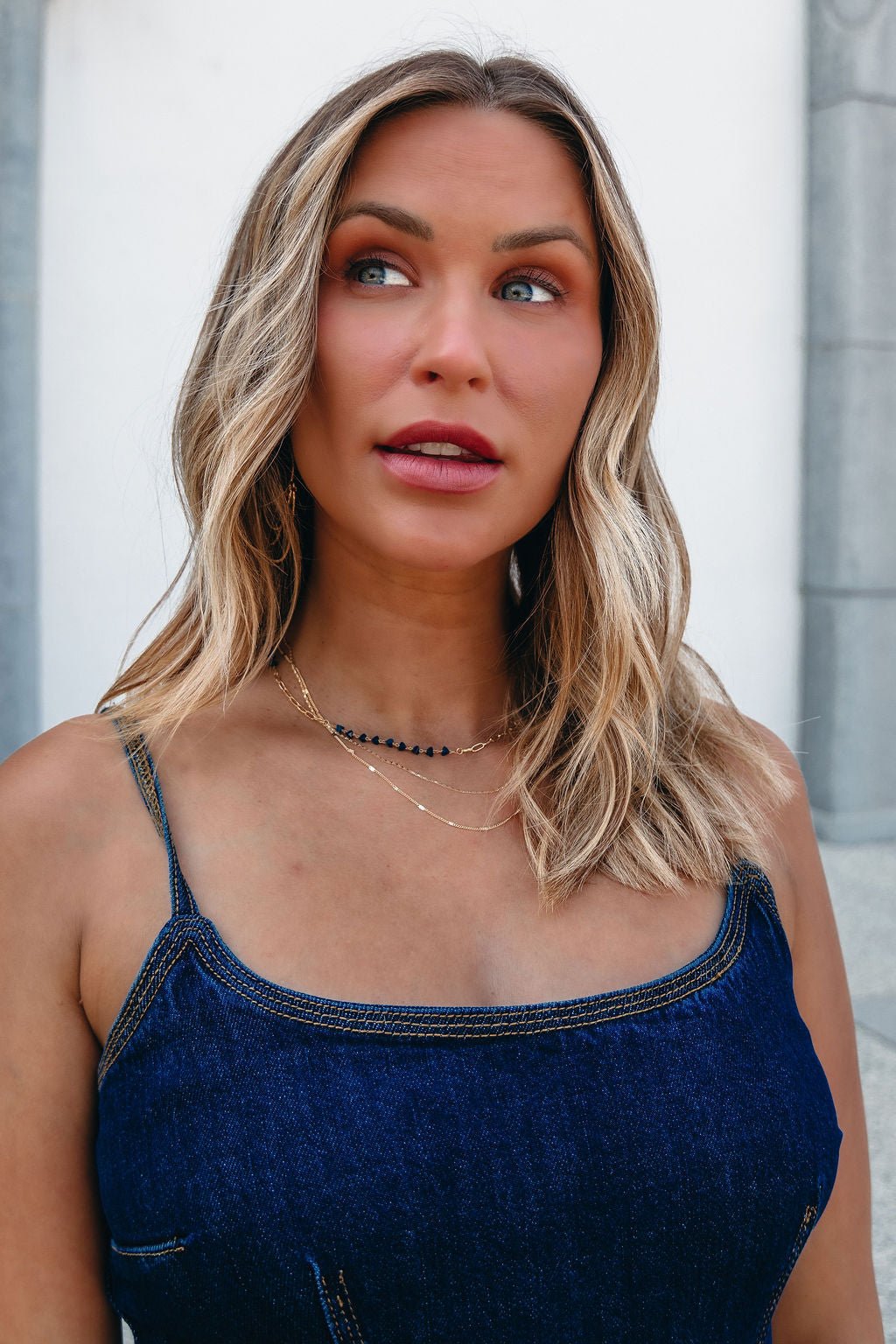 Woman with wavy blonde hair wears the Elegance Layered Chain Link Crystal Necklace (FINAL SALE) outdoors with a denim top.