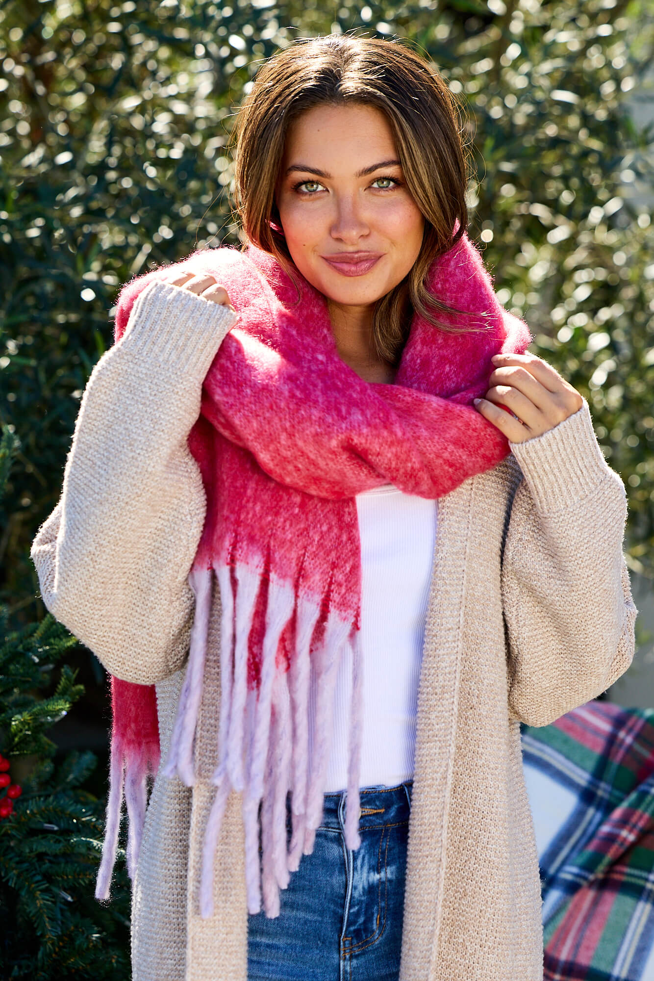 Woman outdoors smiling with greenery, wearing a beige cardigan, white shirt, and Fluffy Red Ombre Fringe Blanket Scarf.
