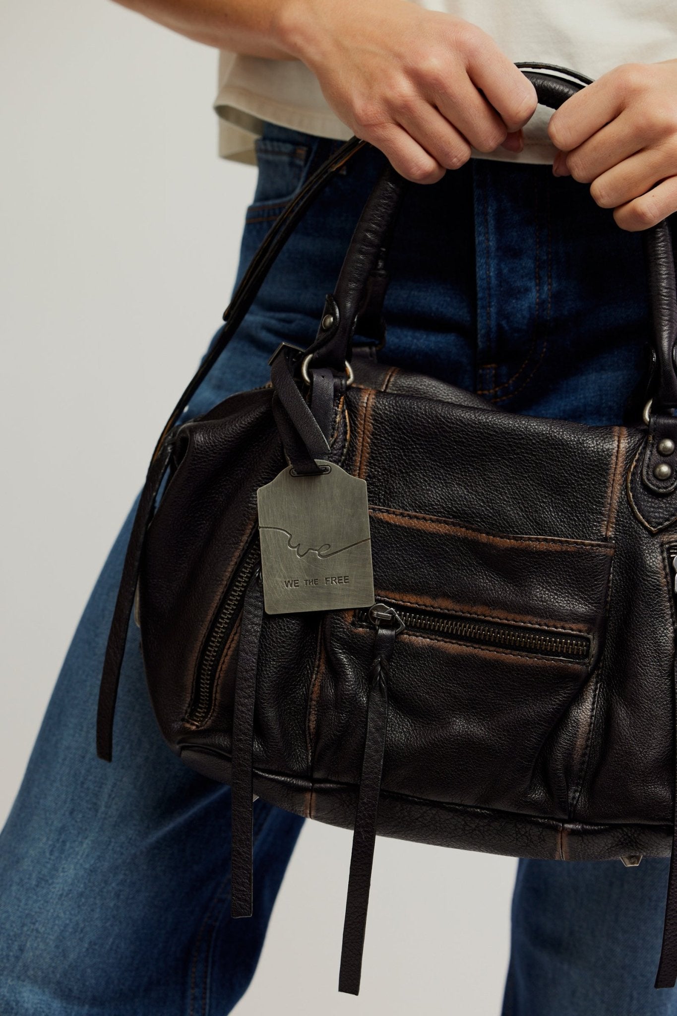 A person holds the Free People Baby Emerson Tote Bag - Black, paired with blue jeans and a white Free People top.