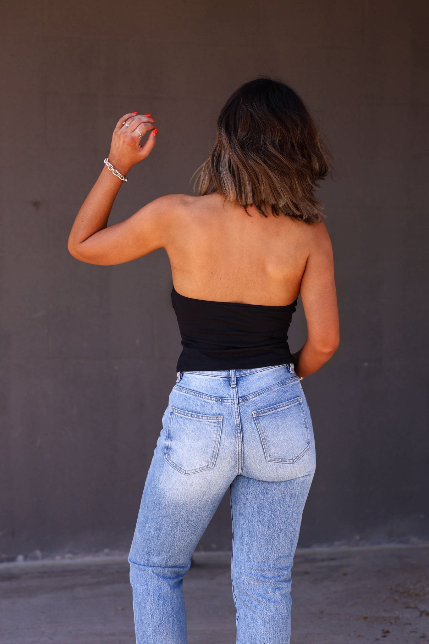 A woman with shoulder-length hair models the Free People Black Still Here Halter Top, paired with light blue jeans against a dark wall.