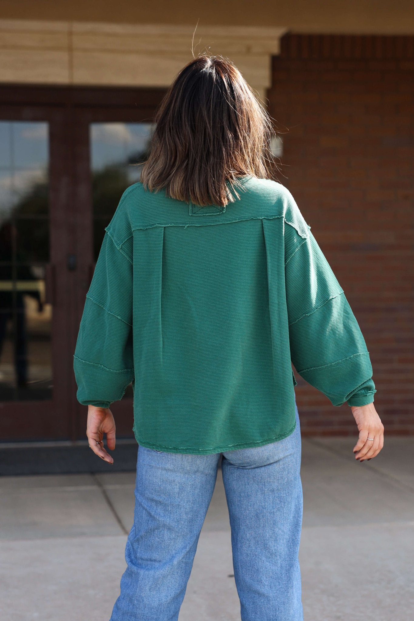Someone wearing a Free People Forest Green Total Eclipse Tee and blue jeans stands outdoors, facing away from the camera.