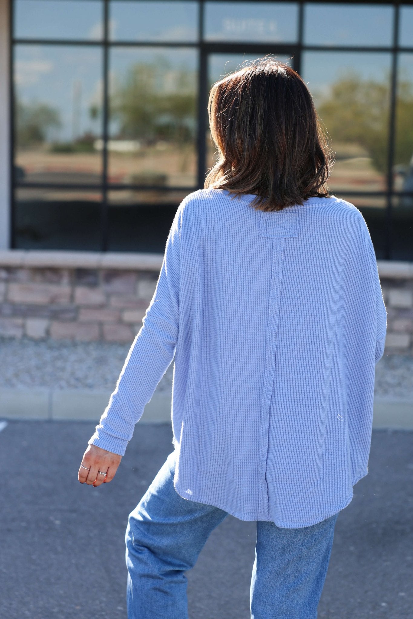 A woman outdoors, back to camera, wears the Free People Latte Blues Solid Thermal Top and jeans.