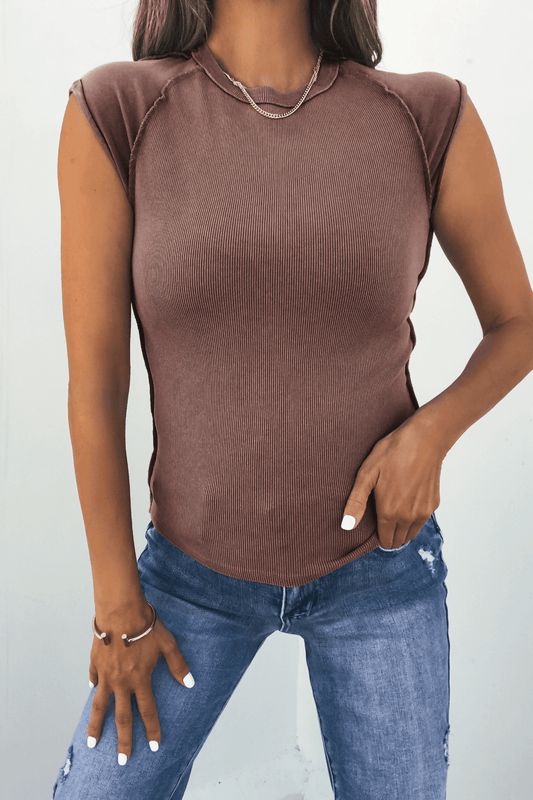 Woman in a Free People Mocha Ever Had Tee, blue jeans, gold necklace and rings, one hand resting on her hip.