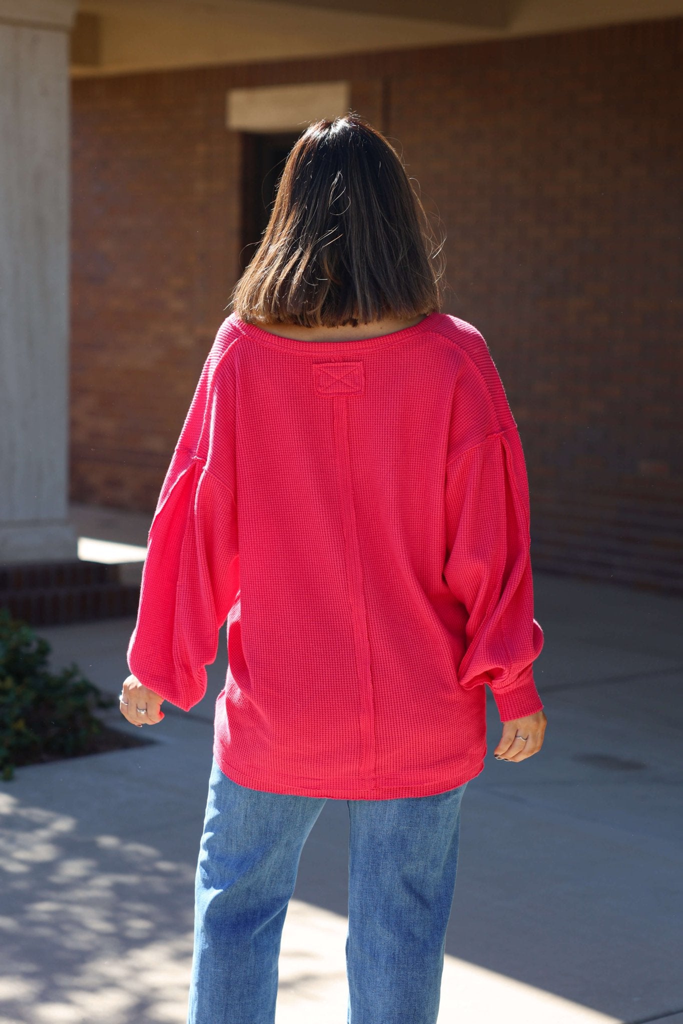 A person with shoulder-length hair wears a loose red Free People Coast 2 Coast Thermal Top and blue jeans, back to the camera.