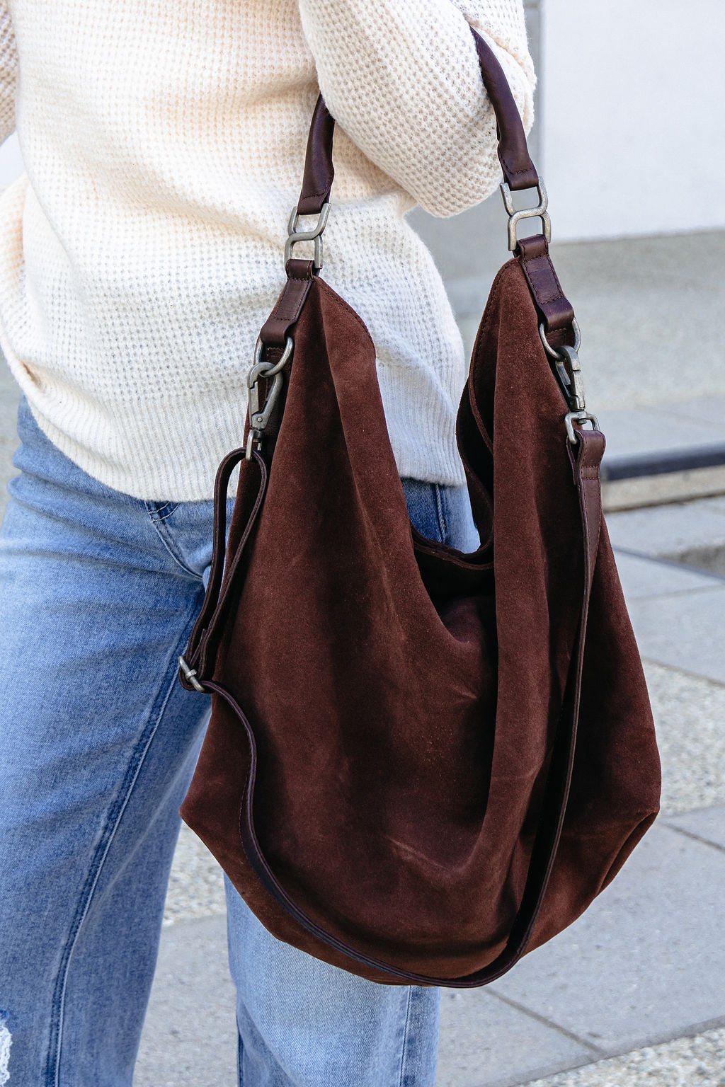 Person in a cream sweater and jeans, carrying the Free People Suzie Suede Tote Bag in brown.