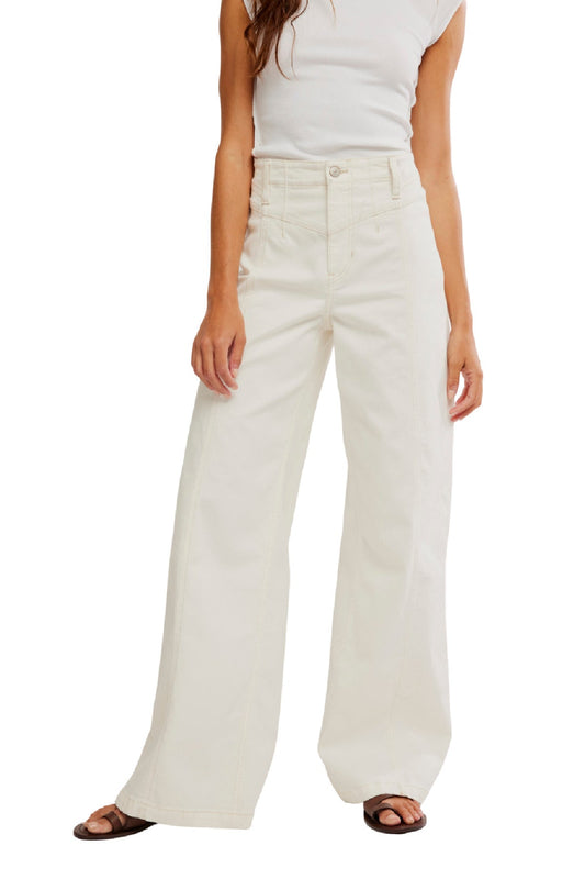 Woman wearing Free People White Libre Wide Leg Jeans - FINAL SALE, a sleeveless white top, and brown sandals against a plain background.