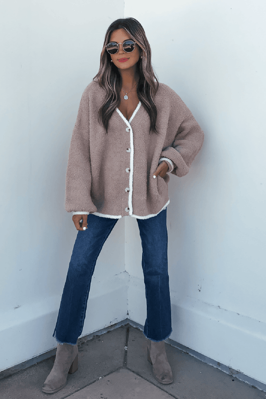 A person wearing a Fuzzy Soft Camel Button Down Cardigan with white trim, dark blue jeans, and ankle boots.
