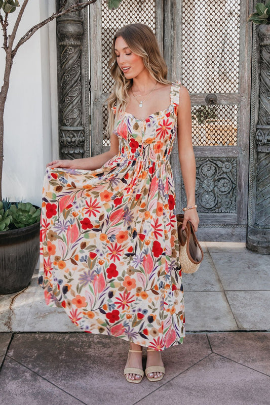 Woman in the Garden Wayfarer Print Midi Dress holds her skirt out, standing before ornate doors with sandals in one hand.
