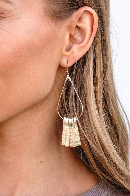 Close-up of a woman wearing Gold Hammered Fringe Teardrop Earrings with layered textured charms.