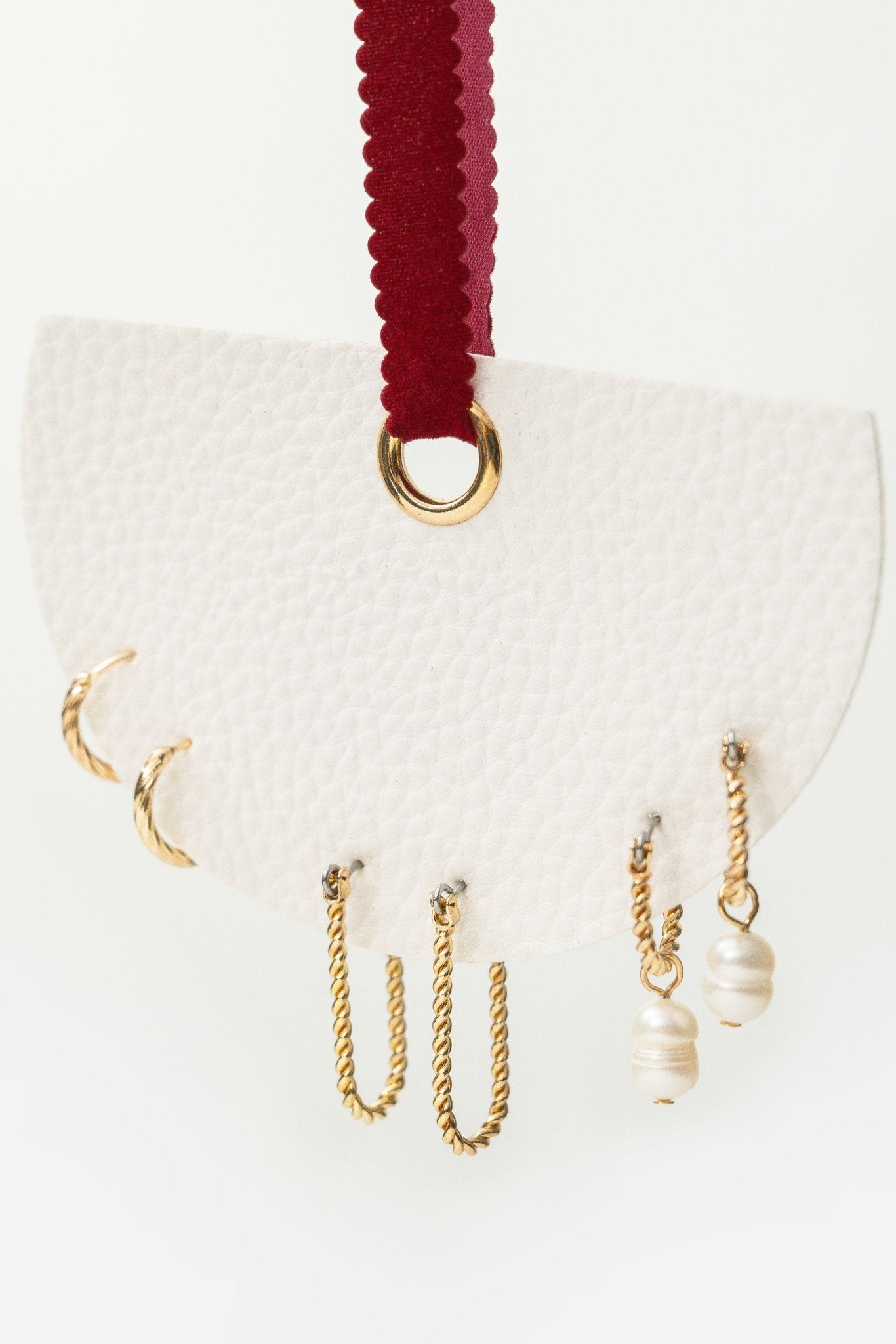 The Gold Pearl Charm Twisted Hoop Earrings Set features five earrings on a textured white card with a maroon ribbon.